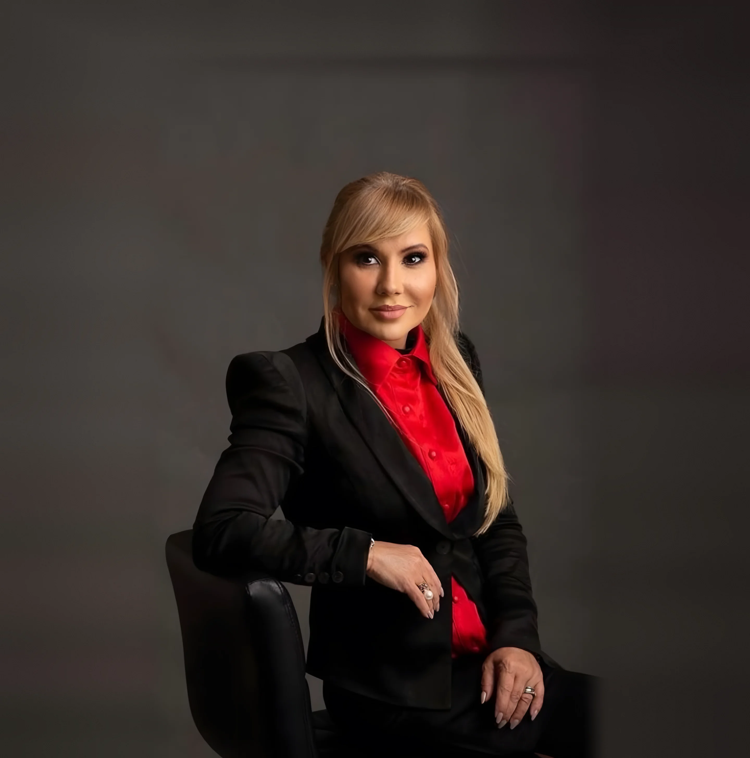 Dra. Flávia Bentes, advogada, sentada em retrato profissional com blazer preto e camisa vermelha