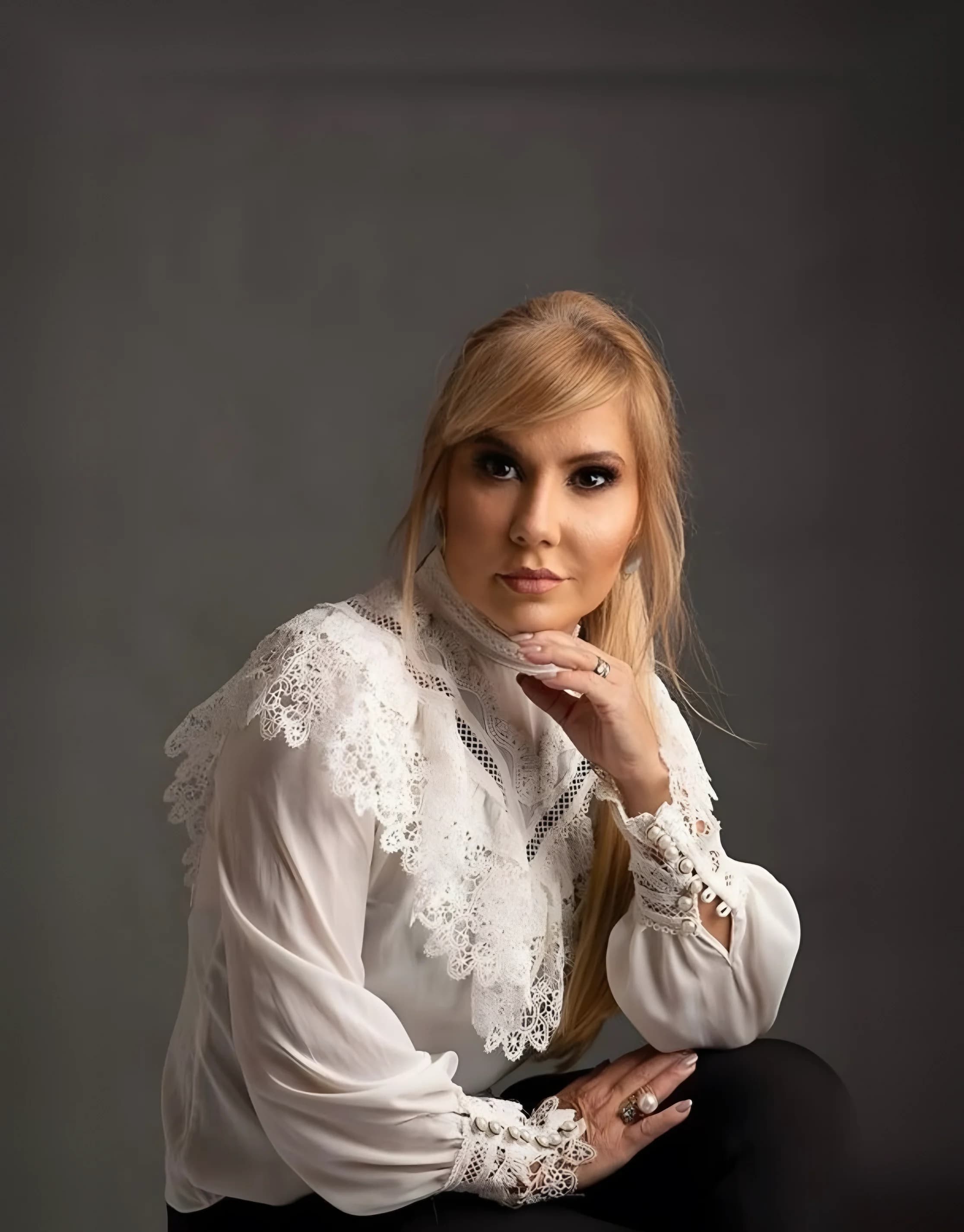 Dra. Flávia Bentes em retrato com blusa branca de renda, mão apoiada no queixo
